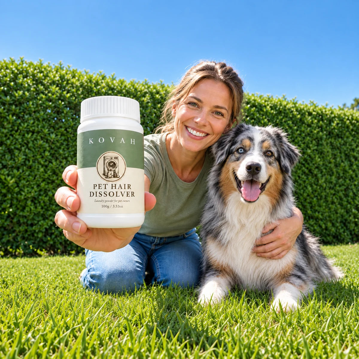 A smiling woman kneeling on the grass with her Australian Shepherd, holding a jar of Kovah Pet Hair Dissolver towards the camera